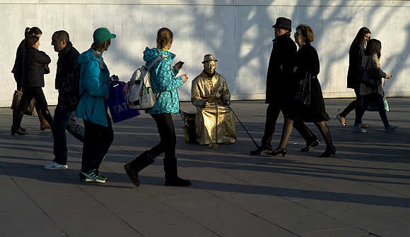 Tourists walk past a street performance artist on the south bank in London.