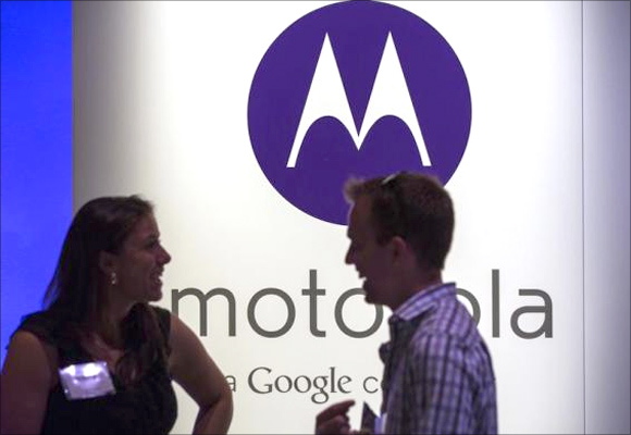 A man and woman laugh in front of a Motorola logo at a launch event for Motorola's new Moto X phone in New York.