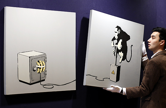 A gallery assistant poses for photographers with British street artist Bansky's diptych work Monkey Detonator at Bonhams auction house in central London.