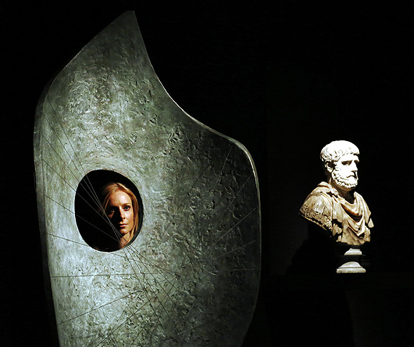 A Christie's employee poses with artworks by Barbara Hepworth Curved Form (L) and one of a pair of polychrome marble busts at Christie's auction house in London.