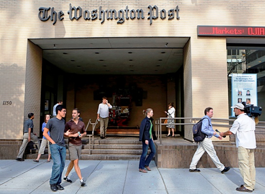 A television cameraman takes up a position as people walk by the entrance of the Washington Post headquarters in Washington.