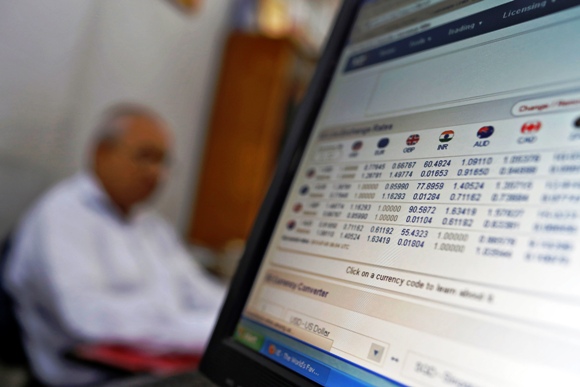 A man sits next to a computer screen showing the Indian rupee currency rates inside a private money exchange office in New Delhi.