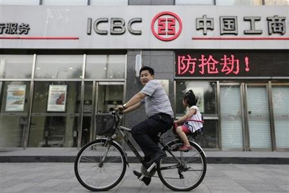 A man cycles a bike carrying his daughter past a branch of Industrial and Commercial Bank of China Ltd (ICBC) in Beijing.