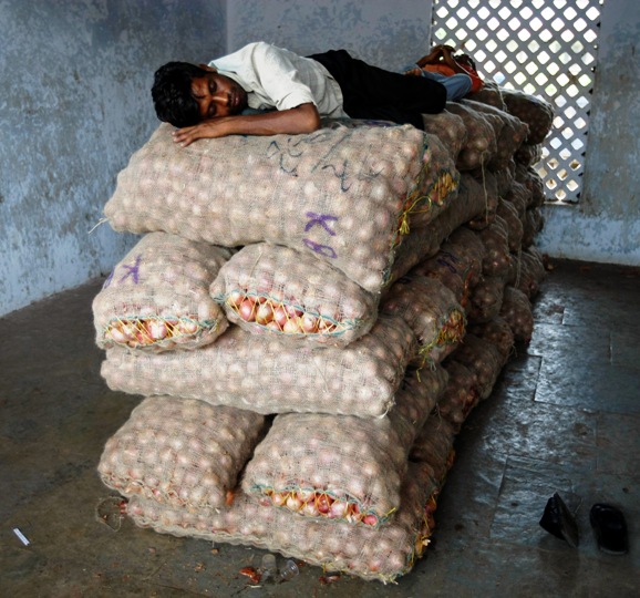 A trader sleeps on sacks of onions at a wholesale market in Ahmedabad.