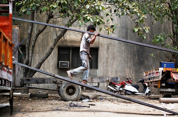 A labourer unloads an iron rod from a truck.