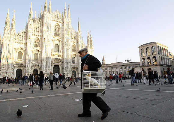 A man carries a cage with a parrot inside it in Duomo Square in downtown Milan.
