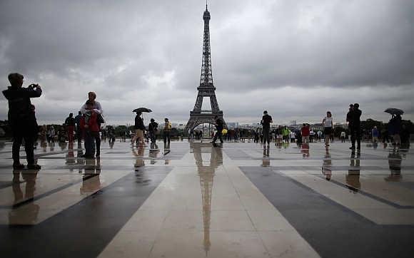 Tourists stroll on the Trocadero square, in front of the Eiffel Tower, during a rainy summer day in Paris.