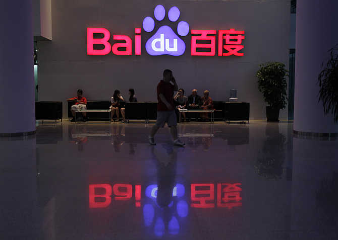A employee uses his mobile phone as he walks past the company logo of Baidu at its headquarters in Beijing.