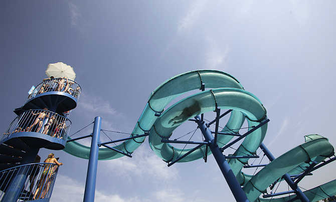 Visitors watch a person sliding down a huge water pipe at a public swimming pool on a hot sunny day in Vienna, Austria.