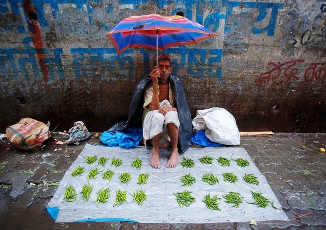 A vegetable vendor sits under an umbrella on a tarpaulin sheet at a market during monsoon rains in Mumbai.