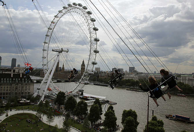 Thrill seekers ride a fairground attraction overlooking the London Eye, Houses of Parliament and the Thames river in London, United Kingdom.