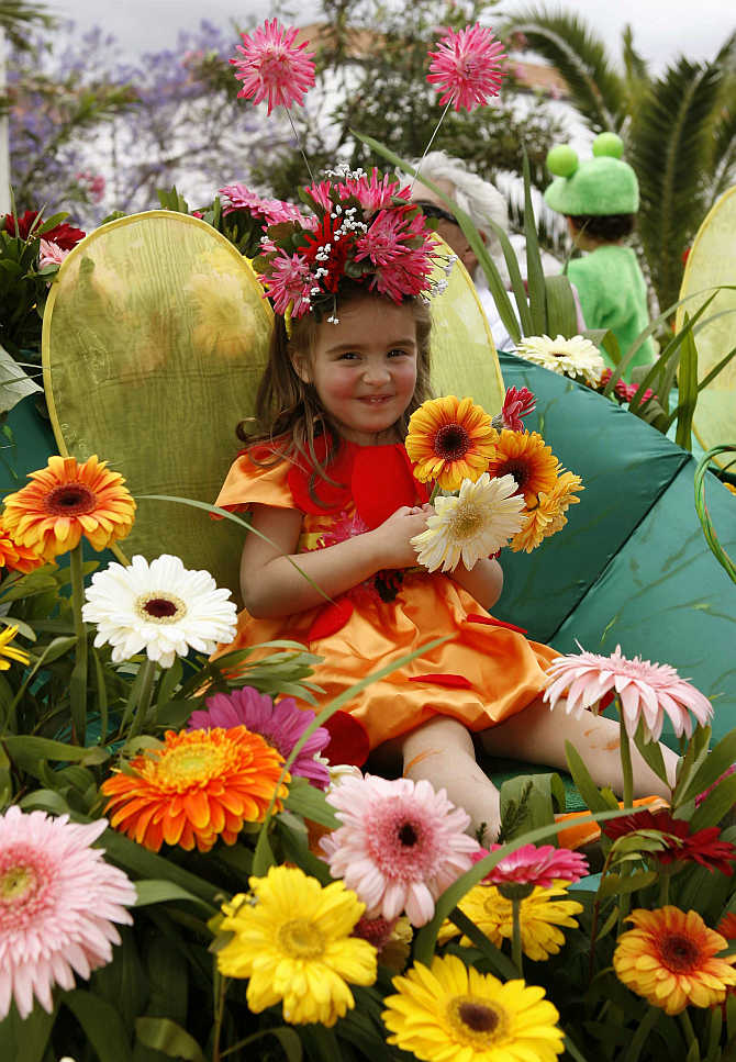 A girl smiles while seated on a float decorated with flowers during a parade at the Madeira Island Flowers Festival in Funchal, Portugal.