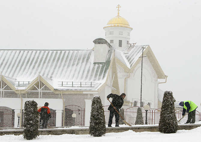 Workers of an Orthodox church clear snow from a pavement in front of the church during heavy snowfall in central Minsk, Belarus.