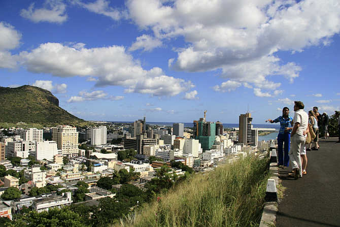 A tour guide stands with a group of tourists at a viewpoint overlooking Port Louis in Mauritius.
