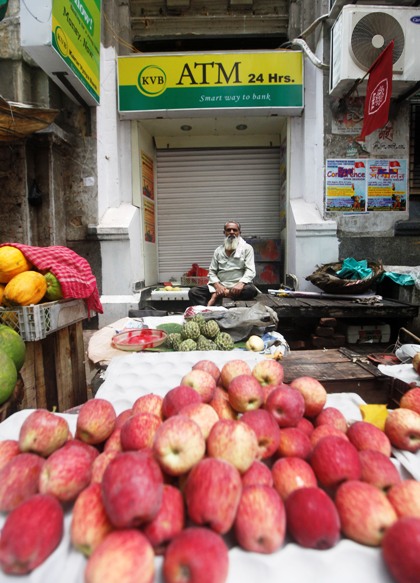 A roadside vendor selling fruits sits in front of a closed automated teller machine counter during a two-day strike in Kolkata.