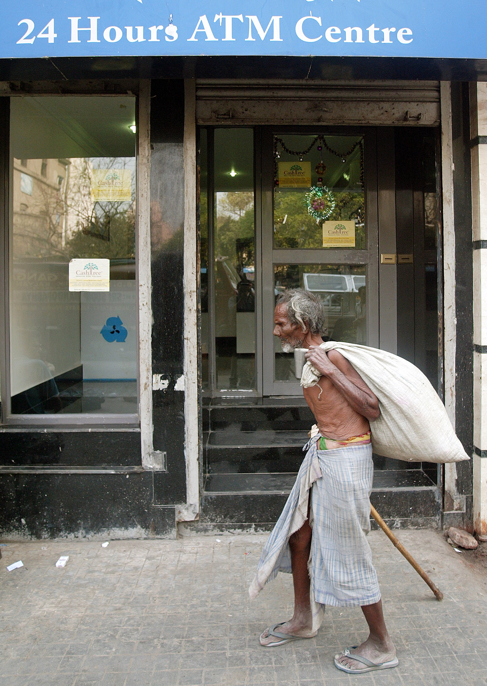 A homeless Indian man walks past a bank's ATM kiosk in Kolkata.