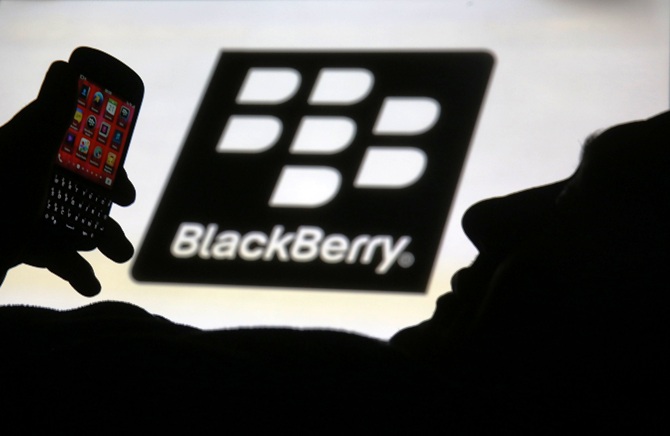 A man is silhouetted against a video screen with the Blackberry logo as he poses with a Blackberry Q10 in this photo illustration.