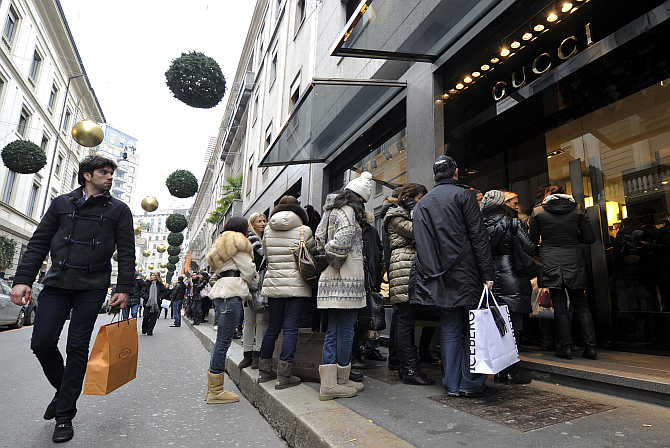 A passer-by looks on as shoppers queue up outside a Gucci shop in downtown Milan, Italy.