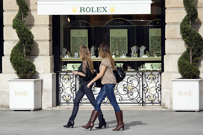 Women walk past a window display of luxury goods maker Rolex in Paris' Place Vendome, France.