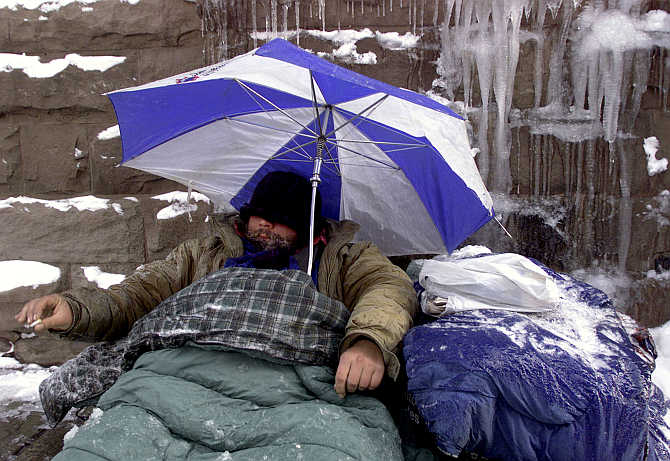 A homeless man uses an umbrella to protect himself from falling and melting ice in Toronto's financial district, Canada.