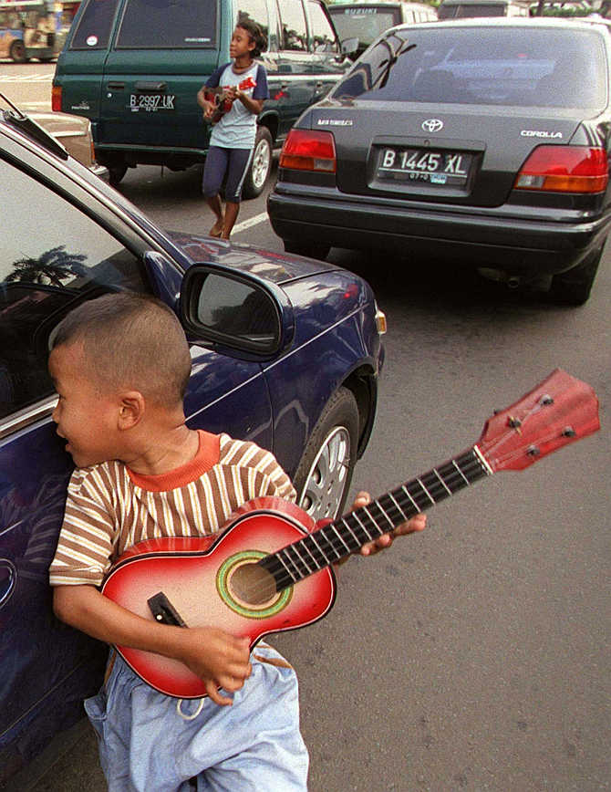 A six-year-old boy carries a small guitar as he begs on the streets of central Jakarta, Indonesia.