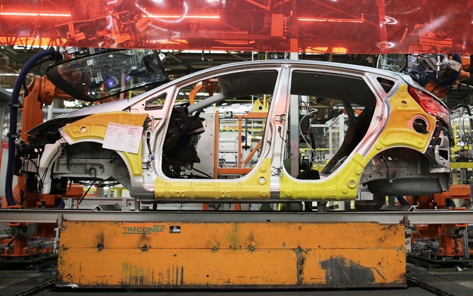 Robot arms assemble windows of a Ford car on an assembly line.