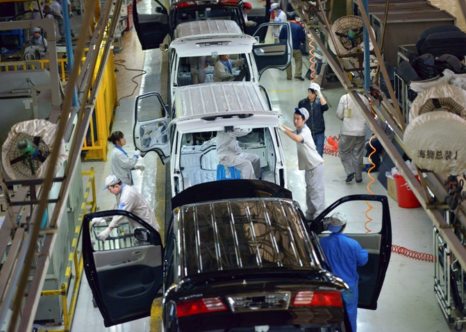 Employees work inside a factory manufacturing automobiles.