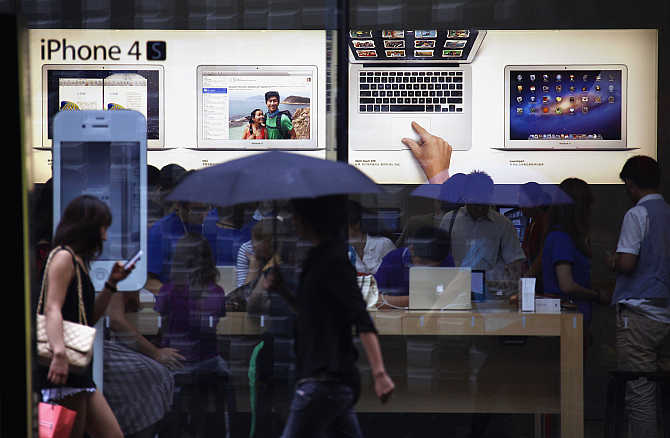 A woman uses an iPhone as she and other pedestrians walk past an Apple store in Beijing, China.