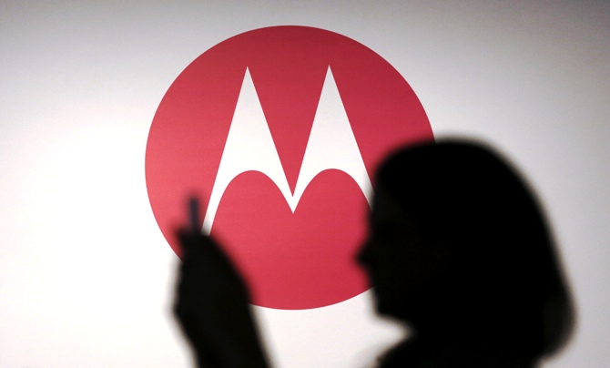 A woman takes a picture in front of a Motorola logo.