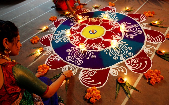 Women arrange oil lamps and flowers around a Rangoli, made from coloured powders, during Diwali in Ahmedabad.