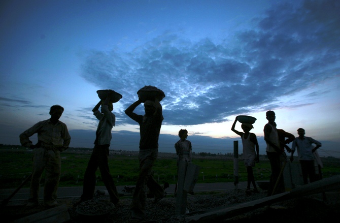 Labourers are silhouetted against the setting sun as they work at a road construction site in Greater Noida on the outskirts of New Delhi.