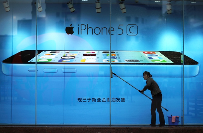 A worker cleans glass in front of an iPhone 5C advertisement at an apple store in Kunming, Yunnan province.