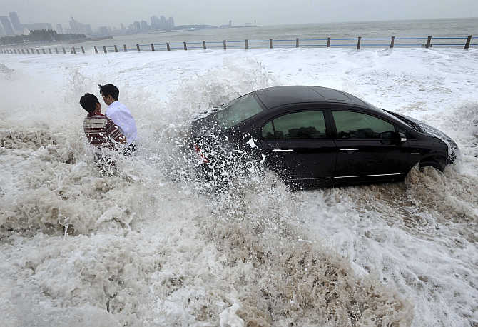Men wait for help by a stranded car on a flooded seaside road as they are surrounded by waves whipped up by typhoon Bolaven in Qingdao, Shandong province, China.
