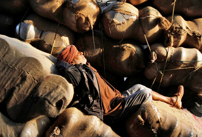 A labourer sleeps on sacks filled with aluminium utensils loaded on a hand cart along a road at a wholesale market in Kolkata.