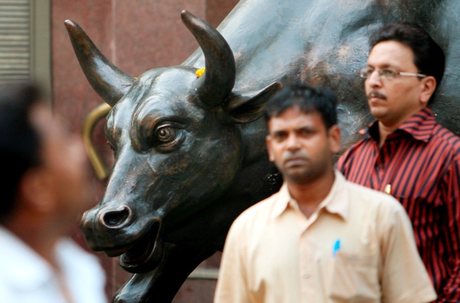 People walk past a bronze replica of a bull at the Bombay Stock Exchange building in Mumbai. 