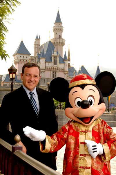 Bob Iger, Chairman and Chief Executive Officer, of the Walt Disney Company, stands next to Mickey Mouse in front of Sleeping Beauty Castle.