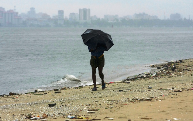 A man strolls along the Fort Kochi beach while holding an umbrella during a rain shower. 
