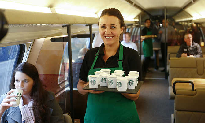 An employee carries a tray with cups of coffee at a Starbucks store aboard a train in Zurich, Switzerland.