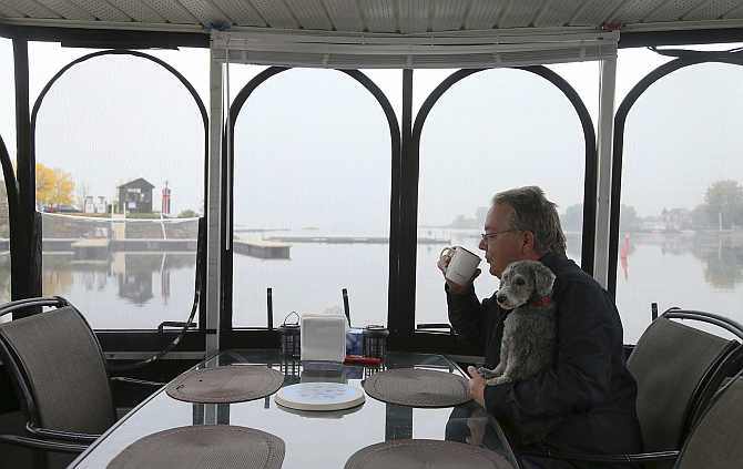 Semi-retired Ian Morton drinks his coffee while holding his dog Zoey onboard his houseboat docked at Le Port De Plaisance de Lachine, a marina in Montreal, Quebec, Canada.
