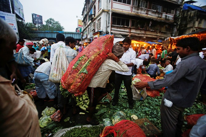 A labourer carries a sack of cabbages after unloading it from a supply truck at a vegetable wholesale market.