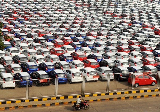 A man rides his motorbike past parked Hyundai cars ready for shipment at a port in Chennai.