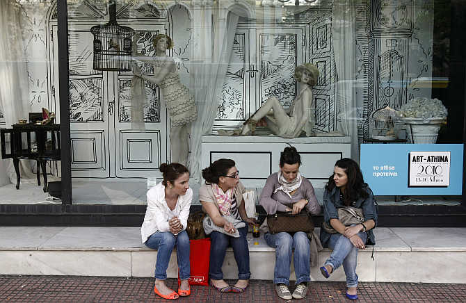 Girls sit in front of a shop window outside a department store in central Athens, Greece.