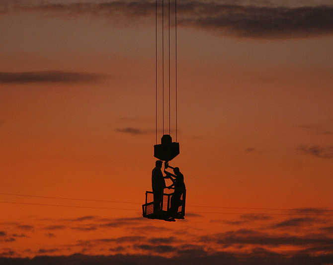 Labourers stand on a winch of a crane at a construction site on the outskirts of New Delhi.