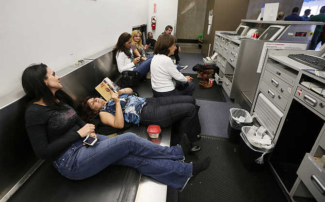 Delayed passengers sit on a baggage conveyer belt at Los Angeles airport in California.