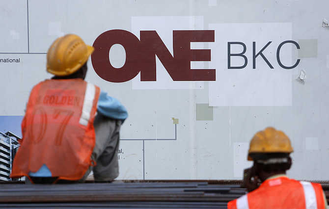 Workers sit in front of an advertising hoarding in the Bandra-Kurla Complex in Mumbai.
