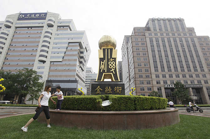 A woman plays with her child next to a statue of ancient Chinese coins at Beijing's Finance Street.