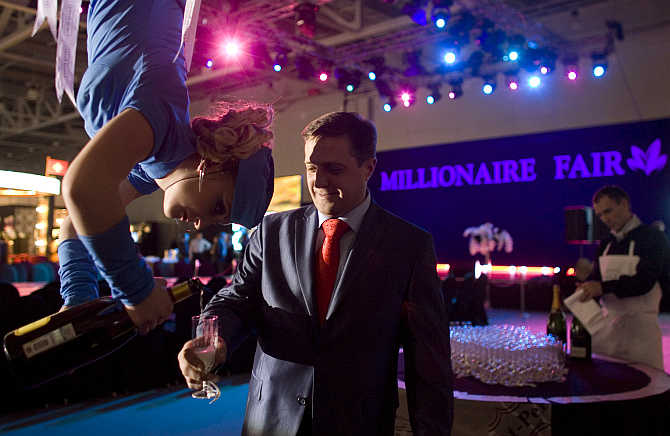 A woman, suspended from the ceiling, serves champagne to a man at the Millionaire Fair in Moscow.