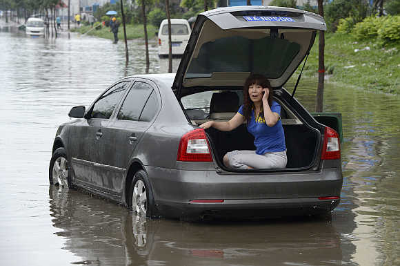 A woman talks on her mobile phone inside the trunk of her car as she waits for rescue on a flooded street in Taiyuan, Shanxi province, China.