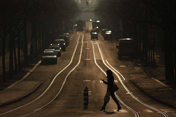 A woman crosses a street while using a mobile phone in Bern, Switzerland.