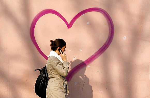 A woman talking on her mobile phone walks past a heart-shaped graffiti in Bucharest, Romania.